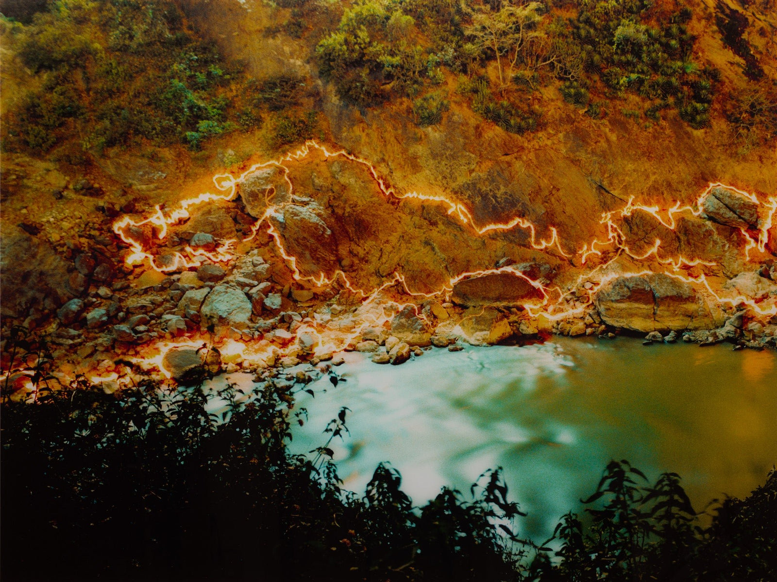 Photographie d’art d’André Wagner: Un cours d’eau turquoise passe entre des rives couvertes de végétation sombre et des rochers brun chaud — Three elements, Indien.
