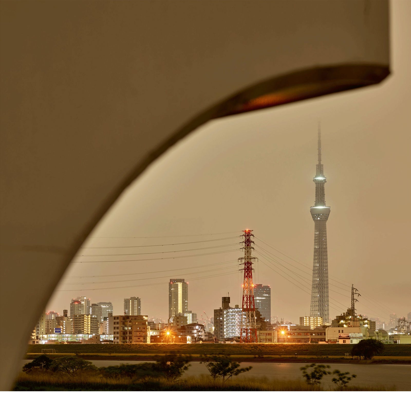Photographie d’art d’André Wagner: Une grande courbe sombre traverse le premier plan et encadre la ville lointaine — Tokyo skyline 1, Japan.