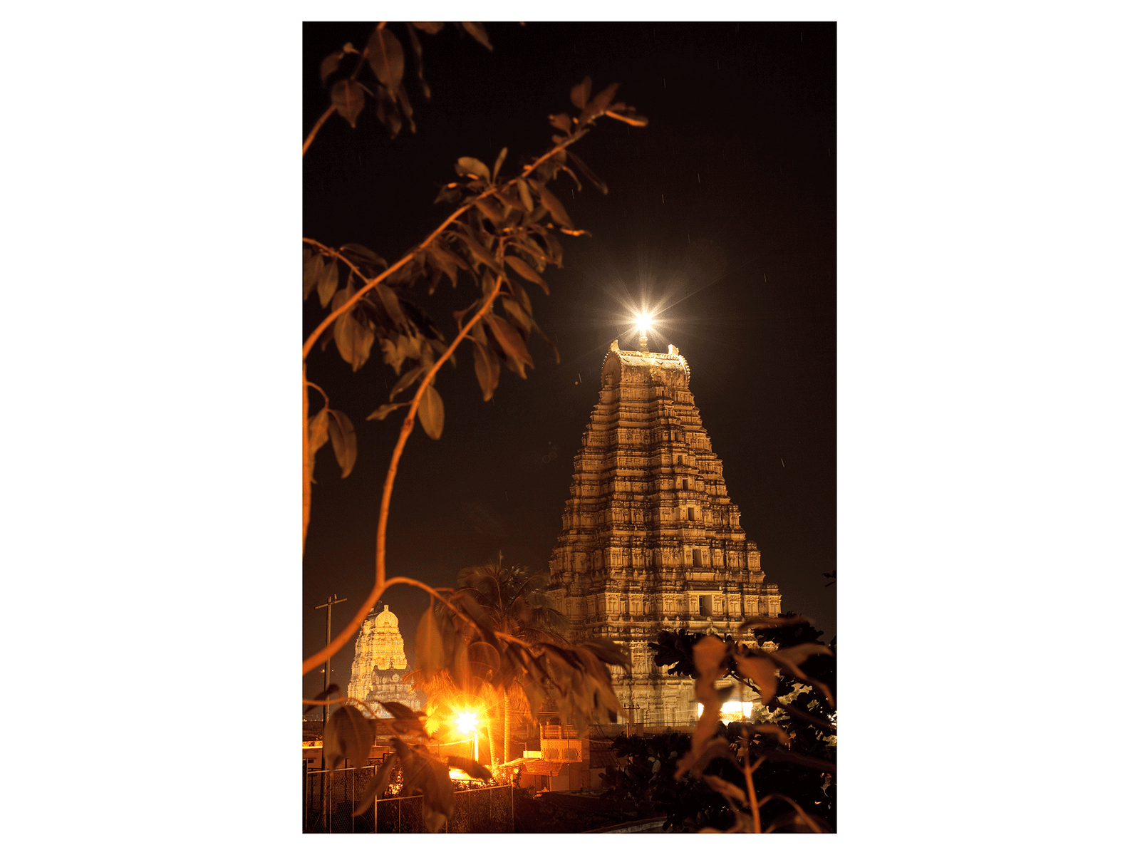Photographie d’art d’André Wagner: Une haute tour de temple se détache, brun doré, sur un ciel presque noir — Virupaksha-tempel bei nacht; hampi, Karnataka, Indien.