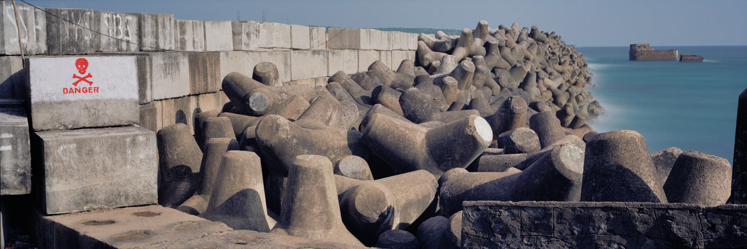 Fine art photography by André Wagner: Multi-armed concrete blocks interlock along a harbour wall, forming an irregular band into the distance — Wave Breakers.