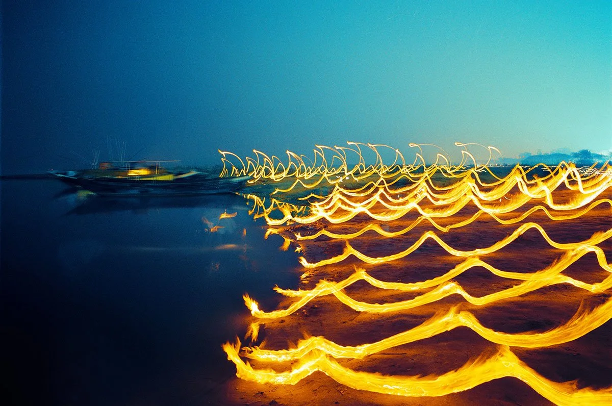 Lumières et bateaux au bord de l’eau, la nuit, dont les contours se dissipent sous l’effet du light painting.