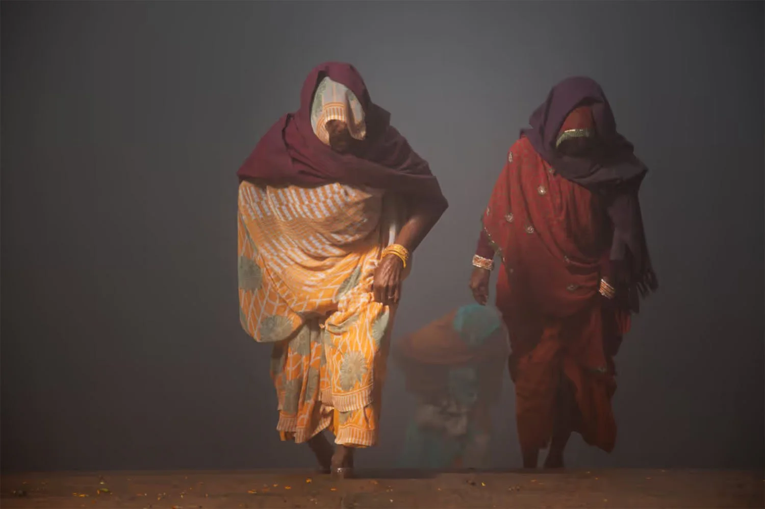 Deux femmes autochtones en vêtements traditionnels traversent pieds nus l’eau, entourées de brume.