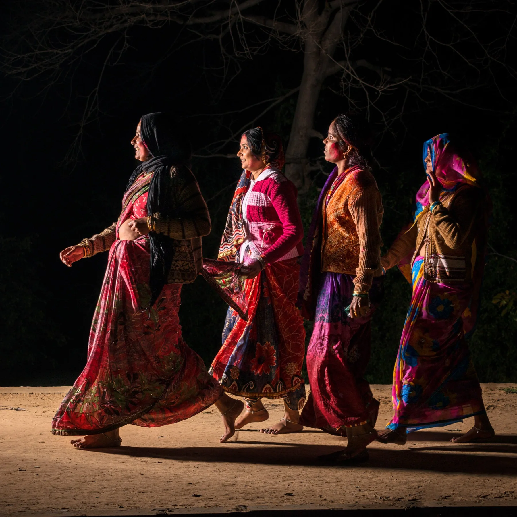 Quatre femmes en vêtements colorés marchent côte à côte la nuit.