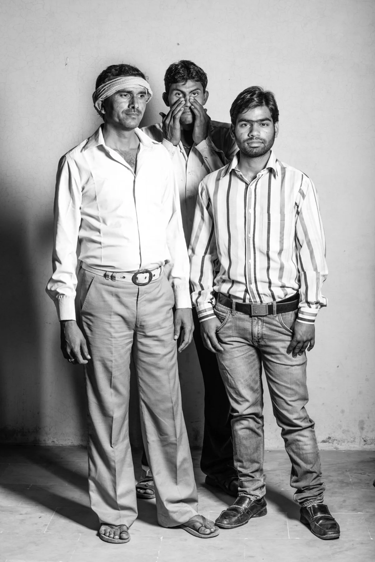 Portrait de groupe en noir et blanc de trois hommes devant un mur clair.