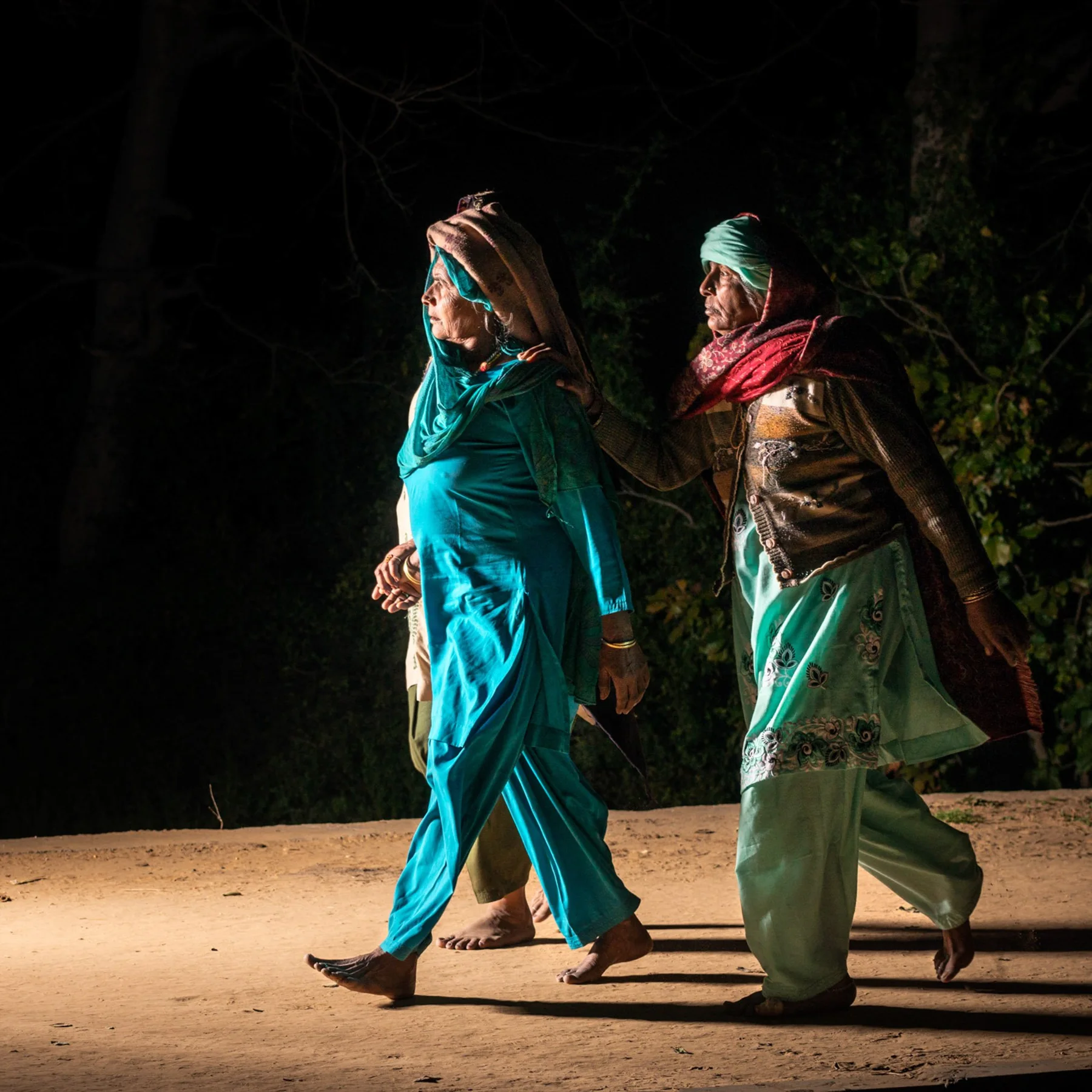Deux femmes en vêtements turquoise et verts dans une rue nocturne.