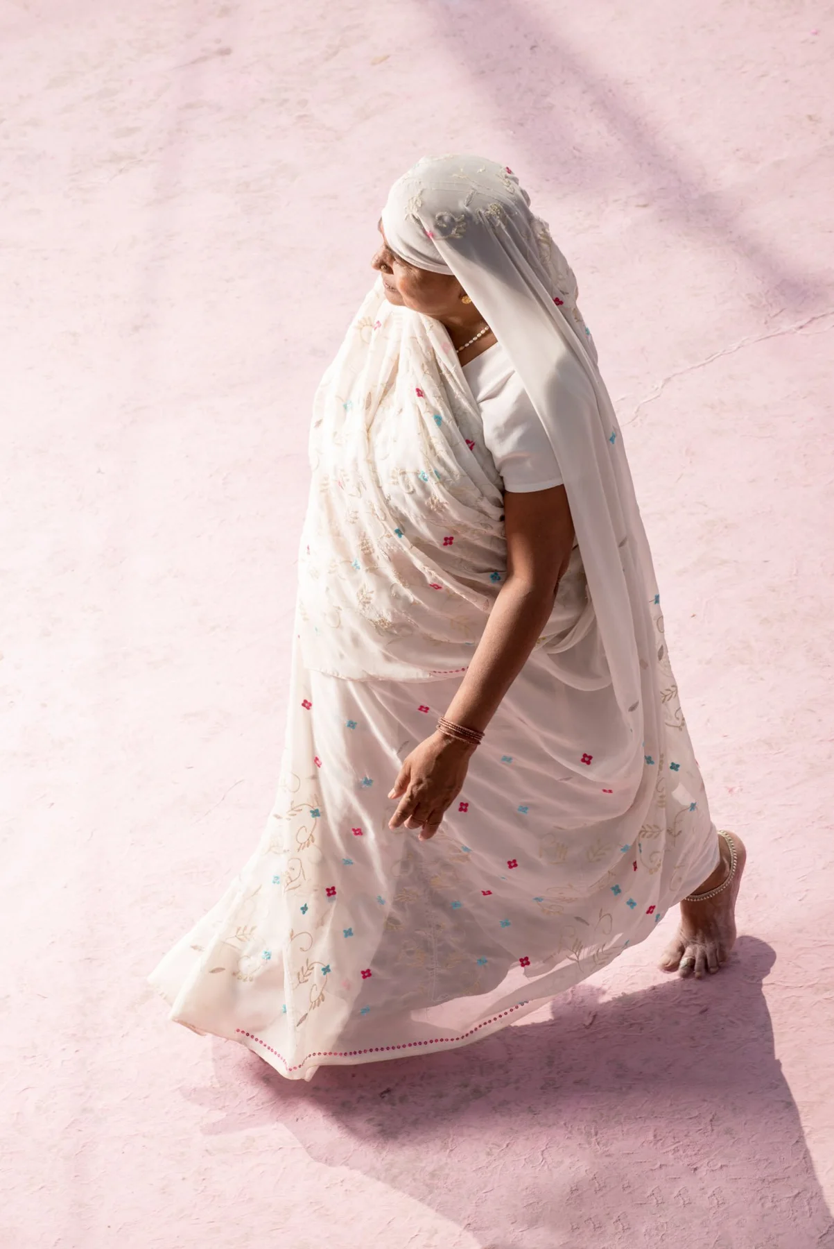Des personnes en vêtements colorés, dont une femme en sari vert, sur un sol teinté de rose.