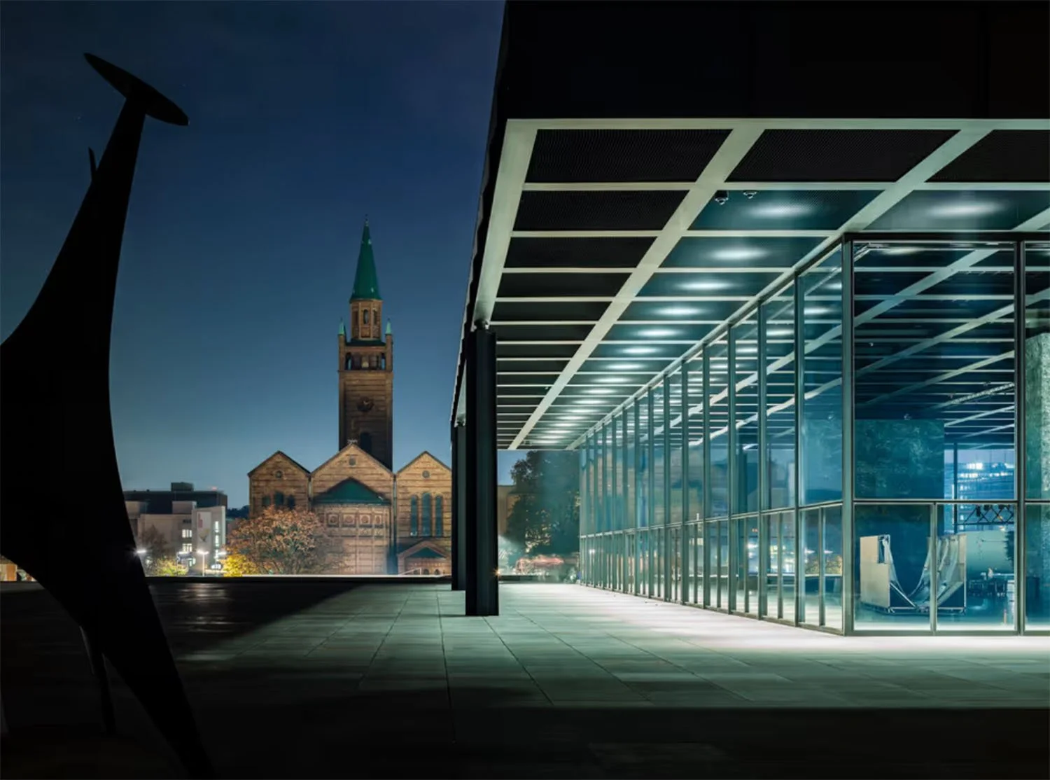 Modern glass facade of a building at night overlooking a historic church in the background.