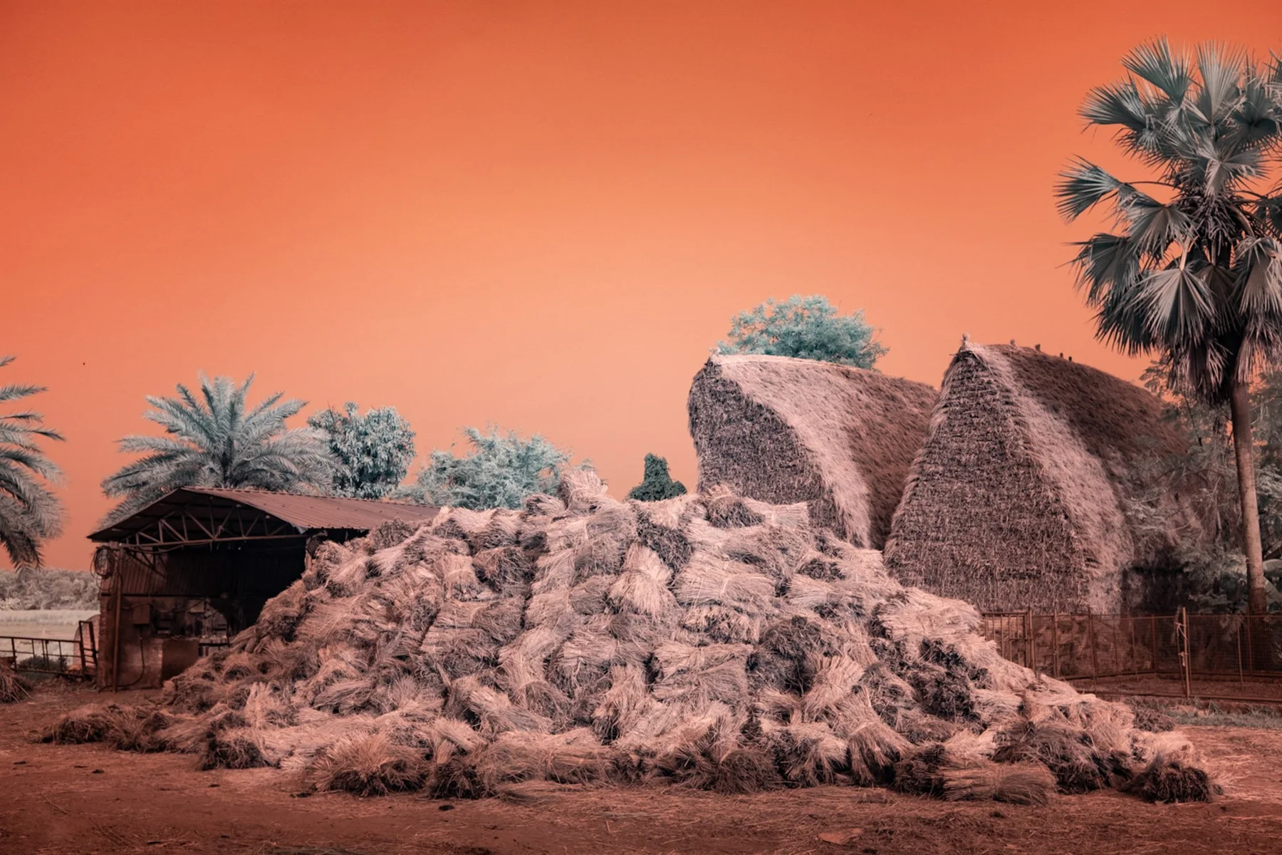 Straw-covered huts and layered material under orange sky.