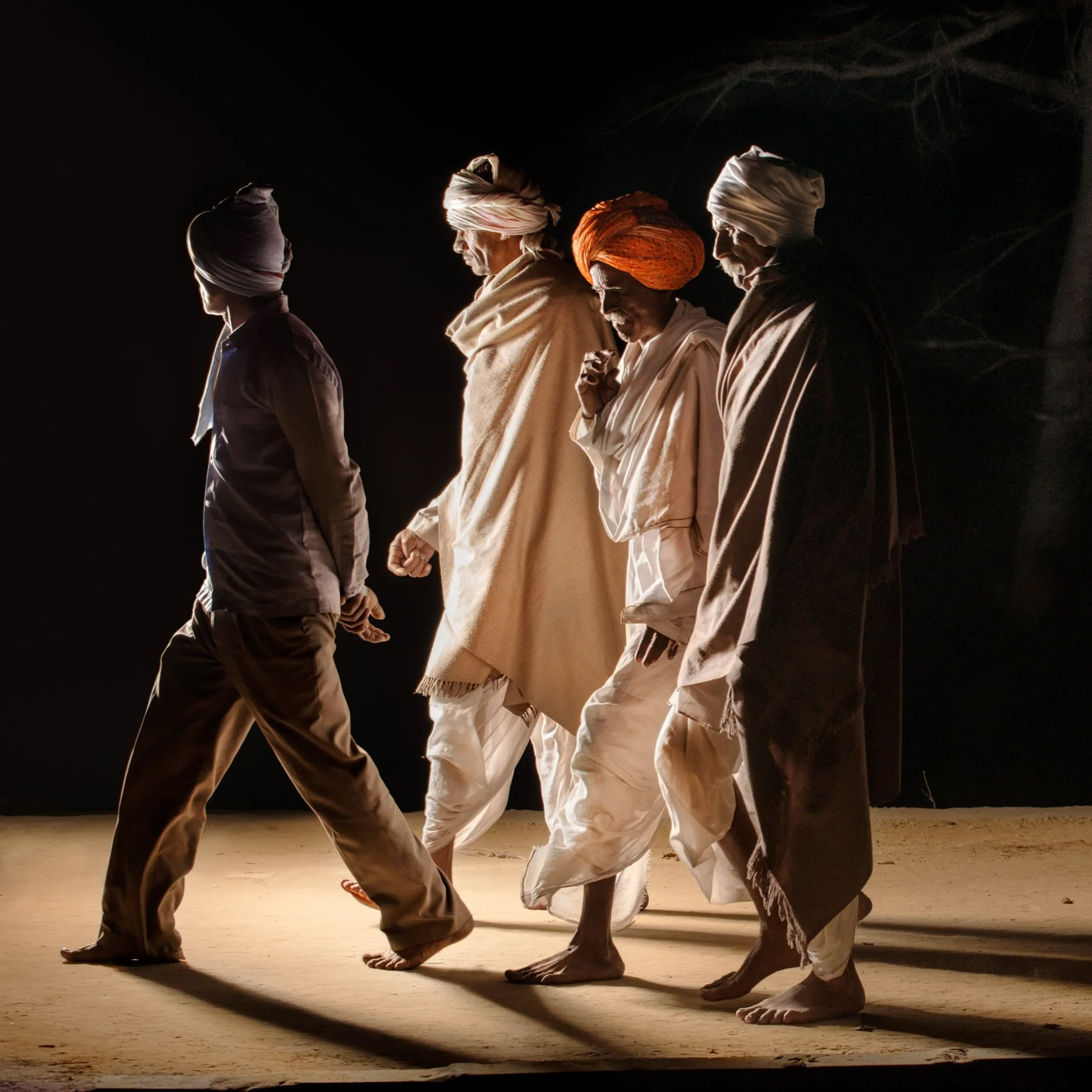 Des hommes en turbans et vêtements clairs marchent ensemble la nuit.