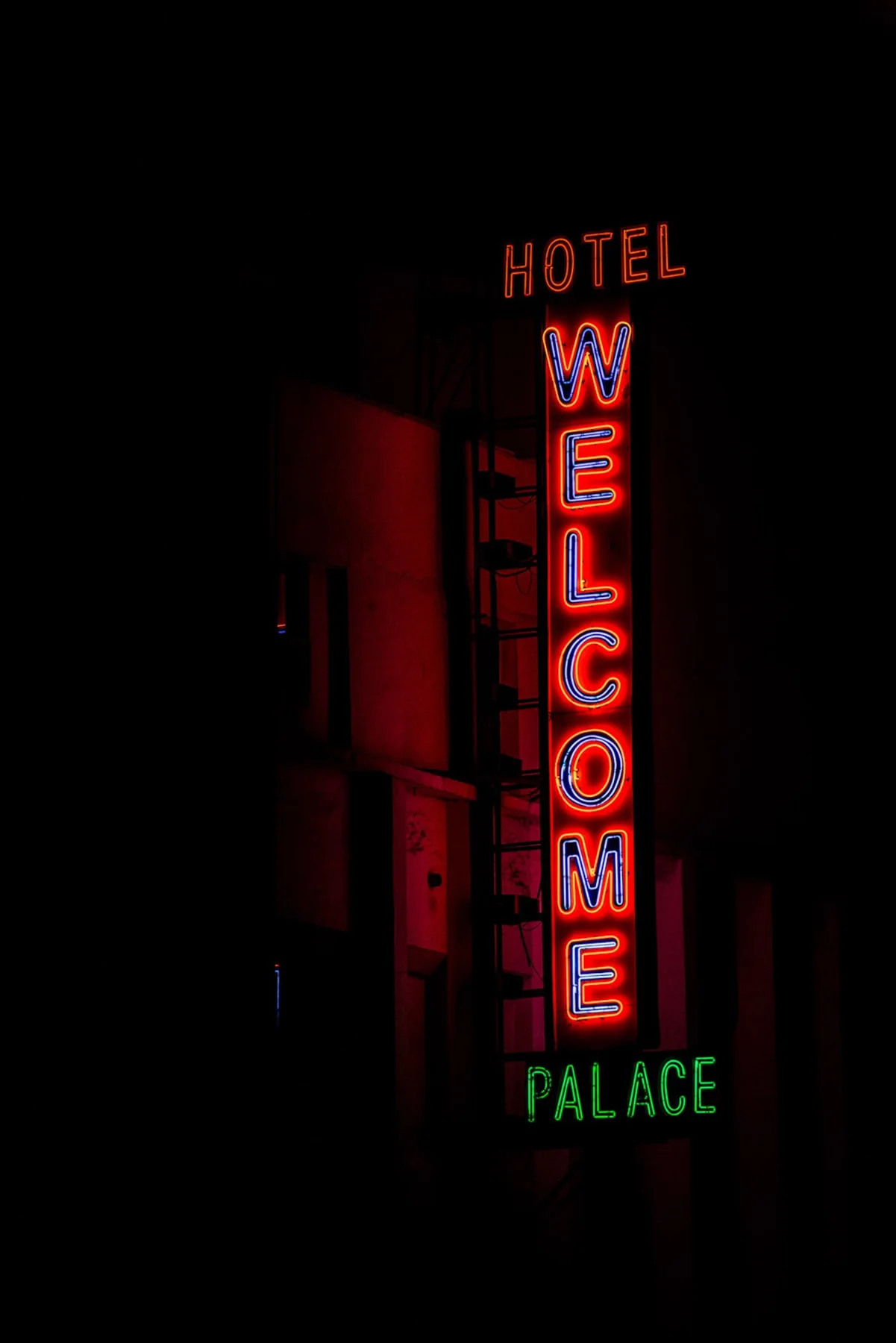 Enseignes lumineuses bleues et rouges sur des bâtiments dans une rue sombre.