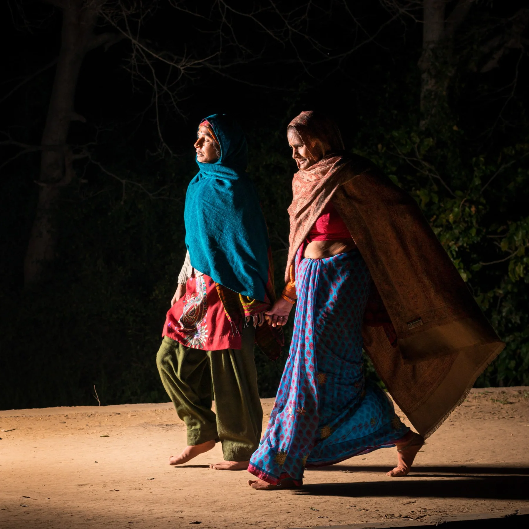 Deux femmes en vêtements colorés marchent côte à côte la nuit.