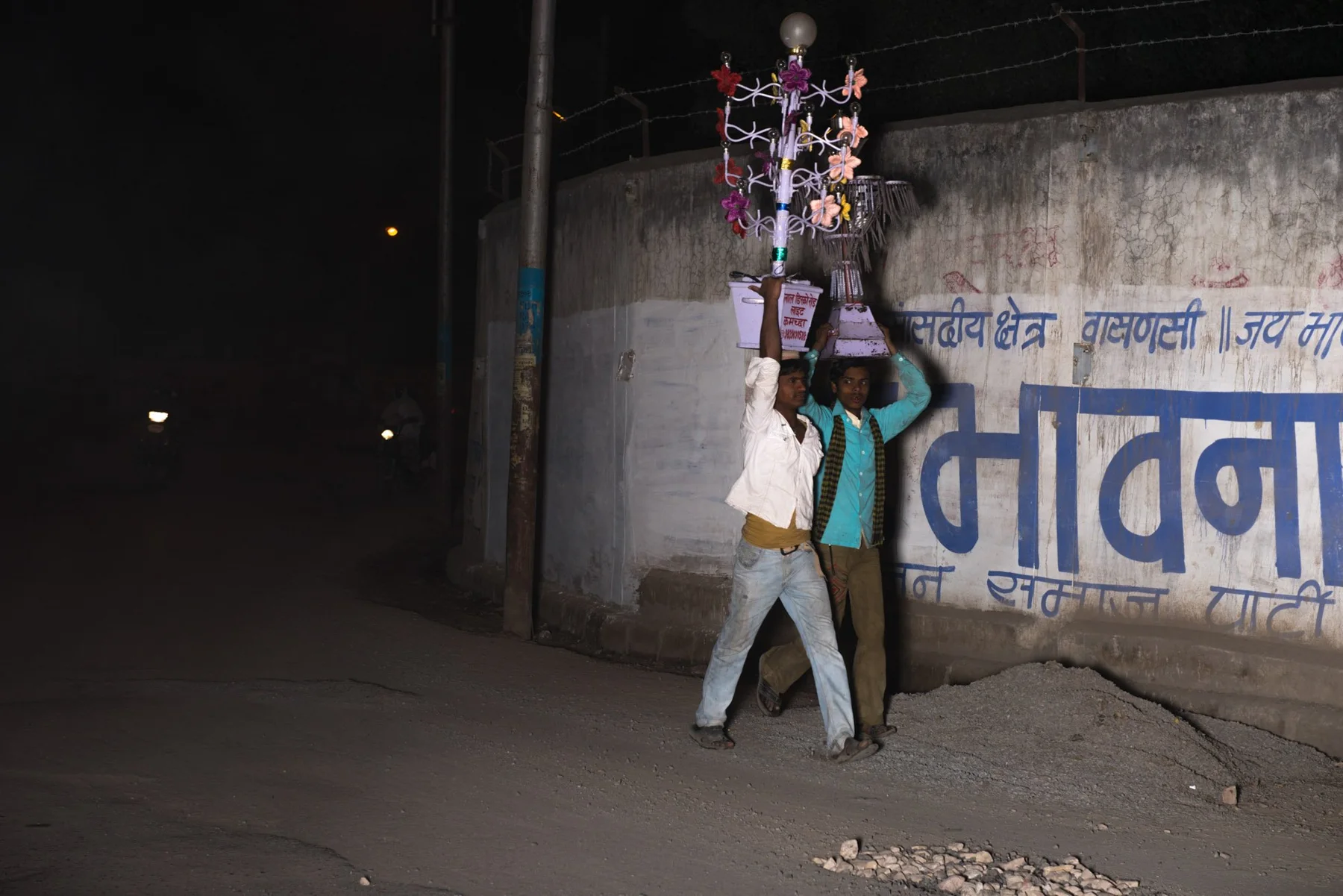 Des personnes portent une haute structure décorée de couleurs dans une rue nocturne.