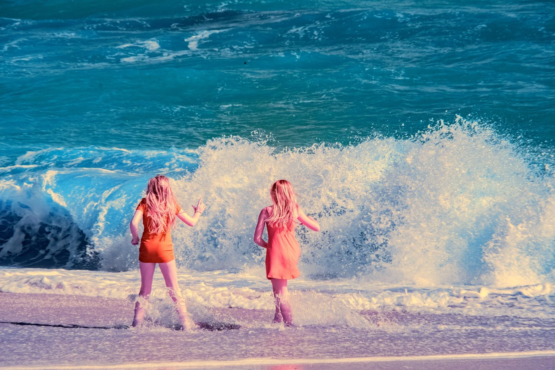 Zwei Menschen am Strand vor einer großen Welle.