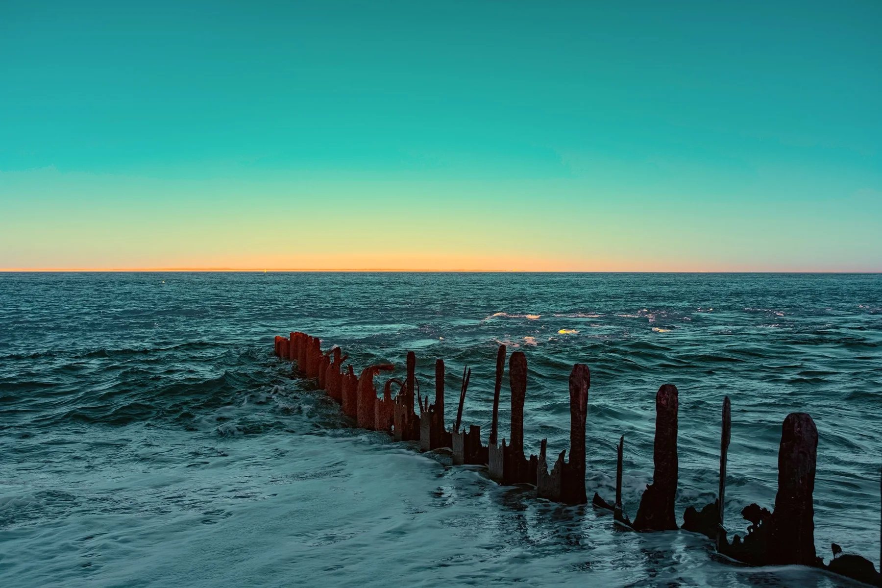 Reihe verwitterter Holzpfähle im Meer.