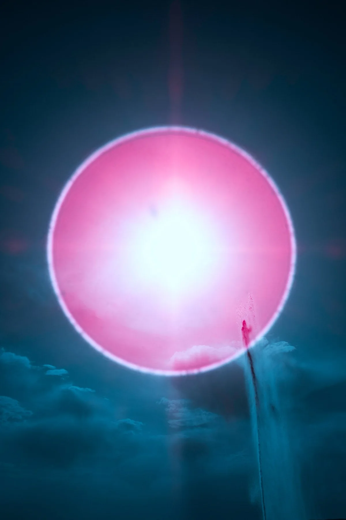 Pink circle of light against blue sky and clouds.