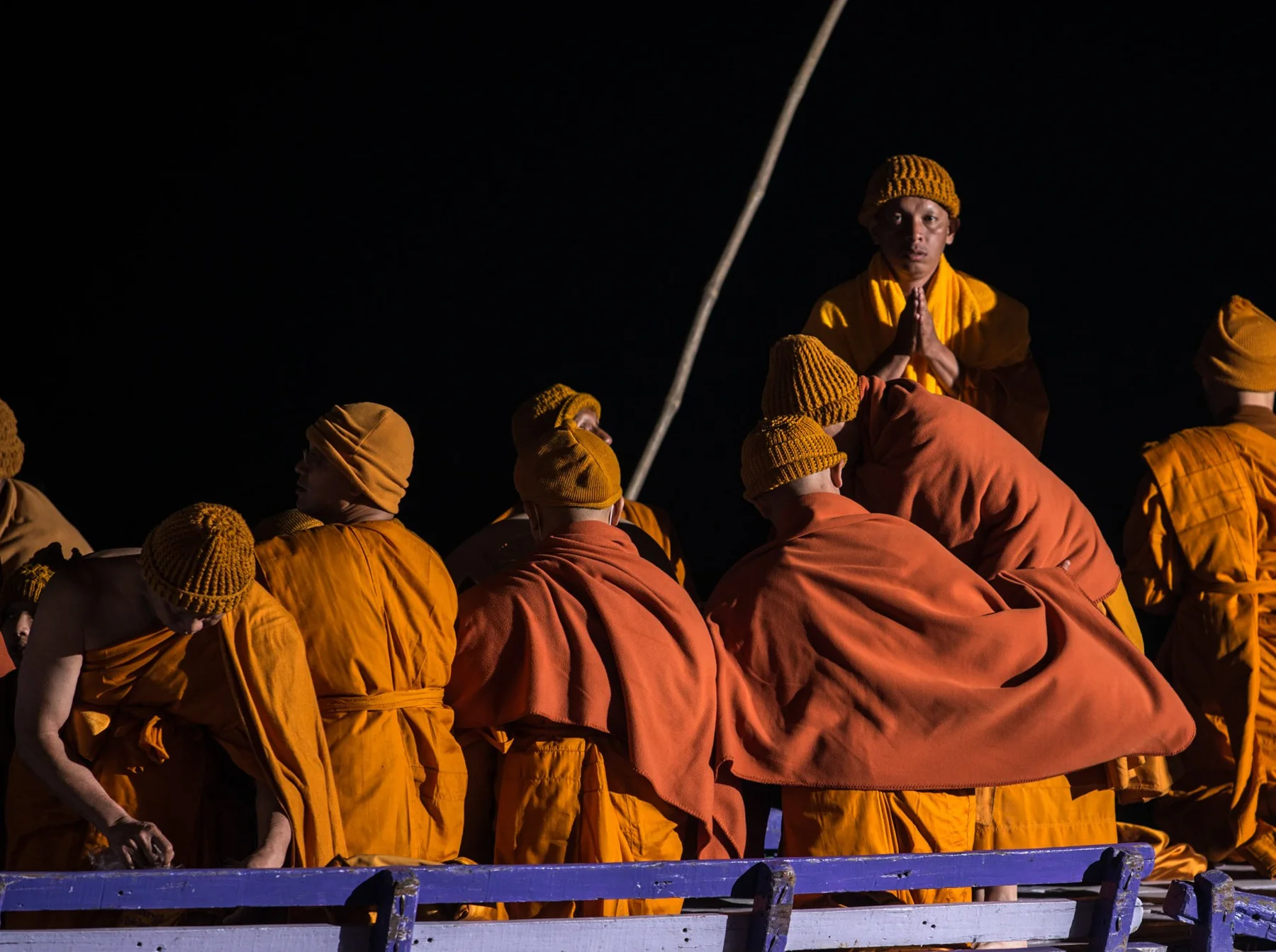 Des personnes enveloppées d’étoffes orange assises sur un bateau la nuit.